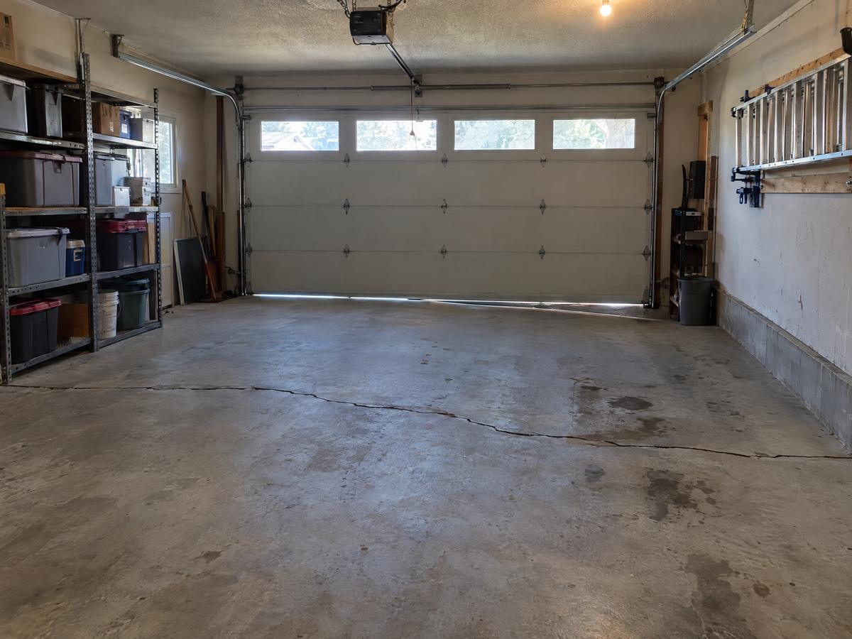 An attached two-car garage where the floor slab has settled toward the door along a crack, with daylight showing under the door seal