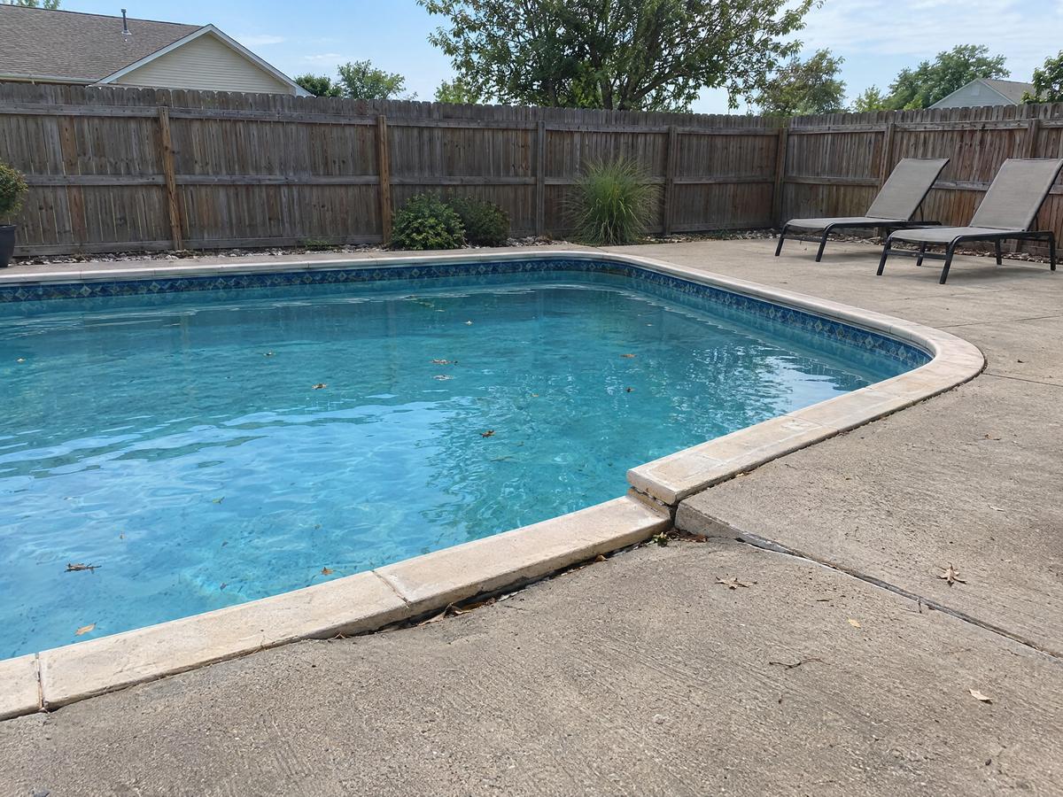 A backyard pool deck where one concrete section has sunk below the coping and the next section, leaving a trip edge, a wood privacy fence behind